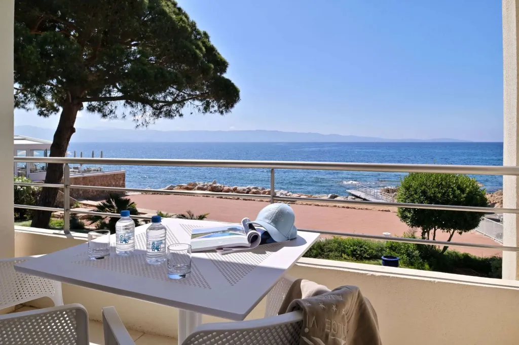 Une table avec des boissons et de la lecture sur une terrasse ensoleillée avec vue sur la mer.