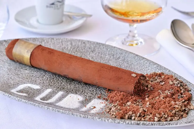 Un dessert en forme de cigare est présenté sur une assiette grise.