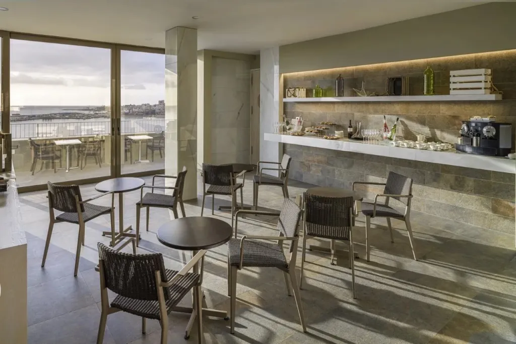 Une salle lumineuse avec des tables et des chaises près d'une grande baie vitrée donnant sur la mer.