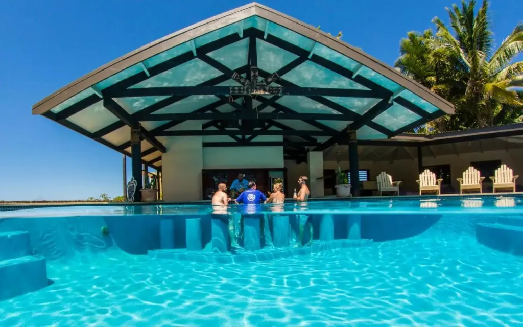 Des personnes se rafraîchissent dans une piscine bordée d'une structure ombragée.