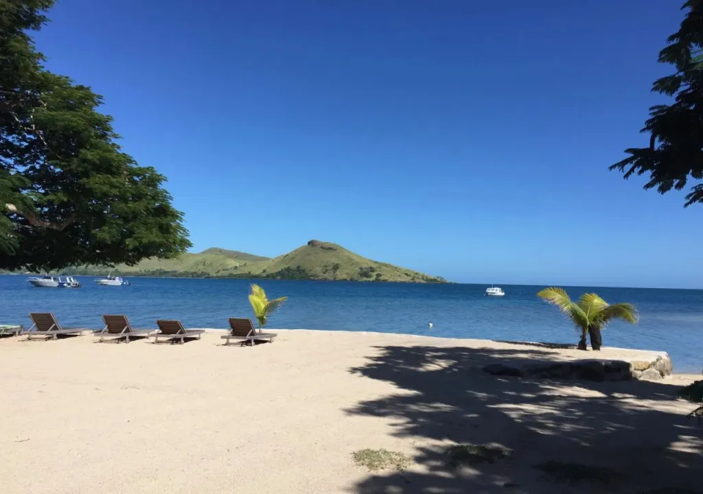 Plage de sable fin avec transats et vue sur la mer et une île.