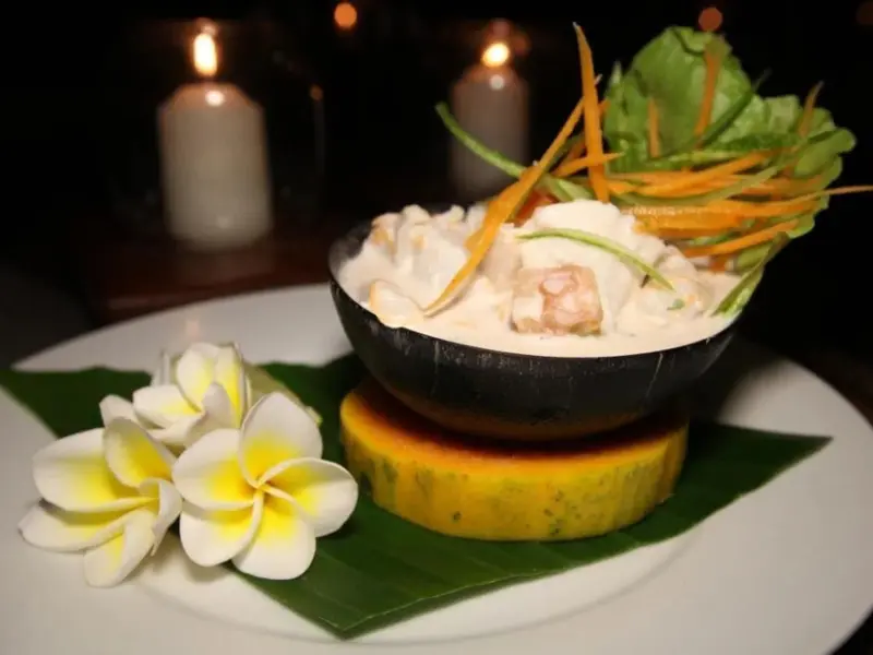 Un plat de crevettes à la sauce crémeuse est présenté sur une assiette décorée de fleurs et de légumes.