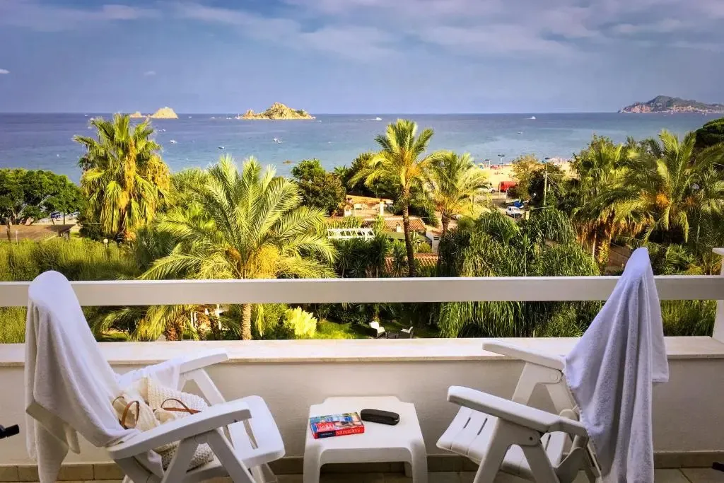 Deux fauteuils blancs sur une terrasse offrent une vue sur la mer et la végétation.