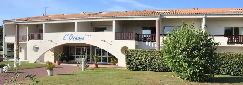Façade d'un bâtiment beige avec des balcons et une entrée arquée.