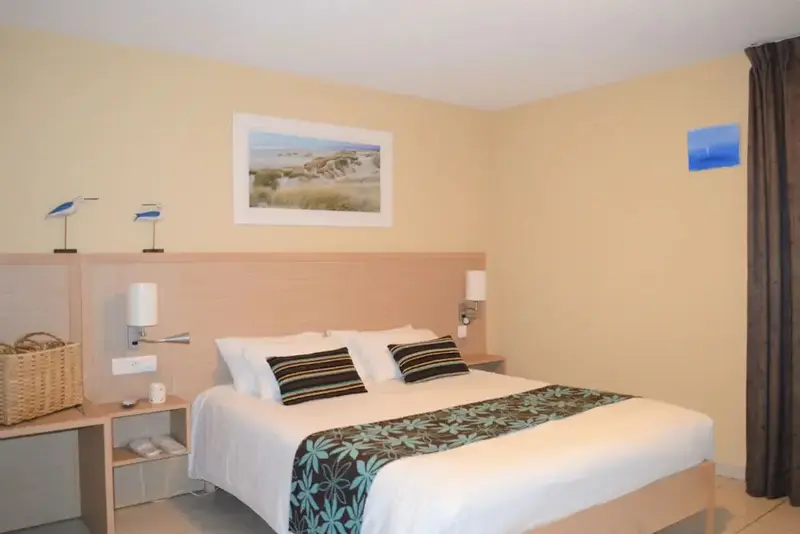 Une chambre lumineuse avec un grand lit recouvert d'une courtepointe blanche et de coussins décoratifs.