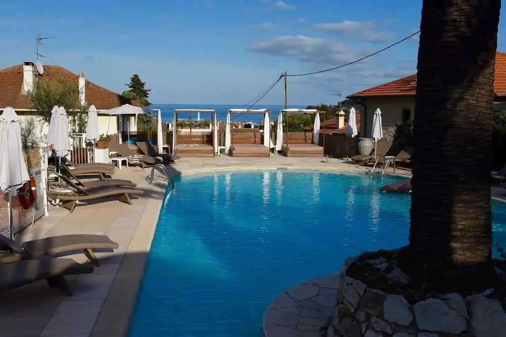 Une piscine bleue bordée de transats et de parasols, avec une vue sur la mer en arrière-plan.