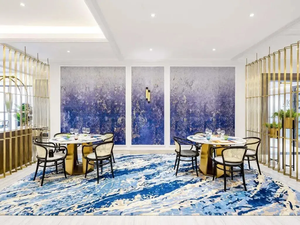 Une salle de restaurant lumineuse avec des tables rondes et un tapis aux motifs bleus.