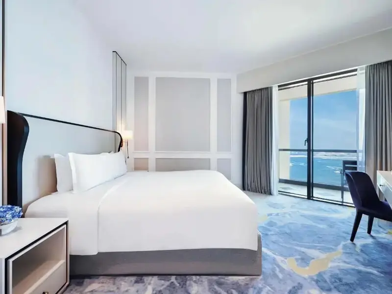 Une chambre lumineuse avec un grand lit face à une baie vitrée donnant sur la mer.