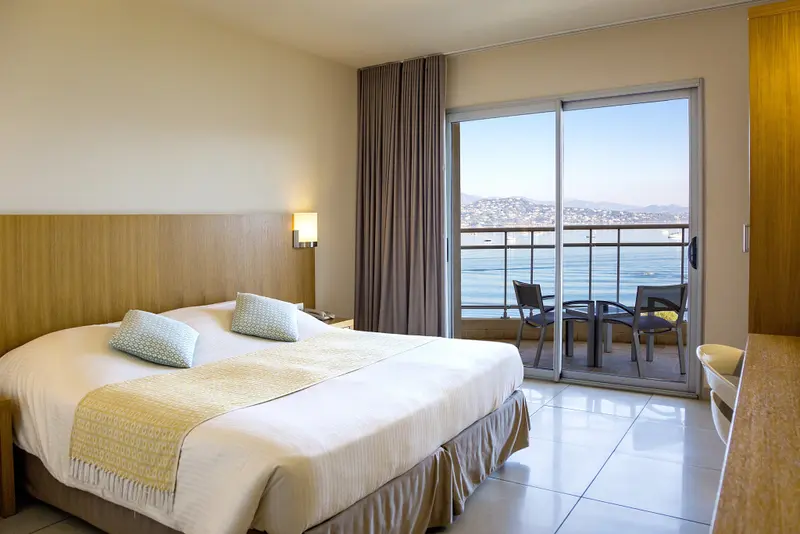 Une chambre lumineuse avec un grand lit donnant sur une terrasse et une vue sur la mer.