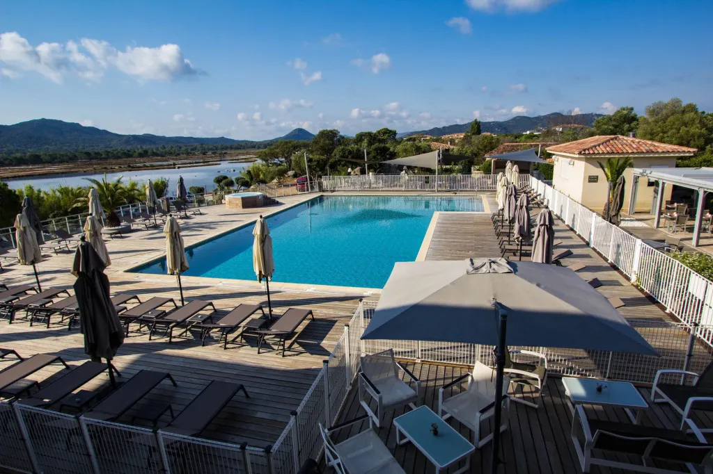 Une piscine ensoleillée avec des transats et des parasols, entourée d'une terrasse en bois.
