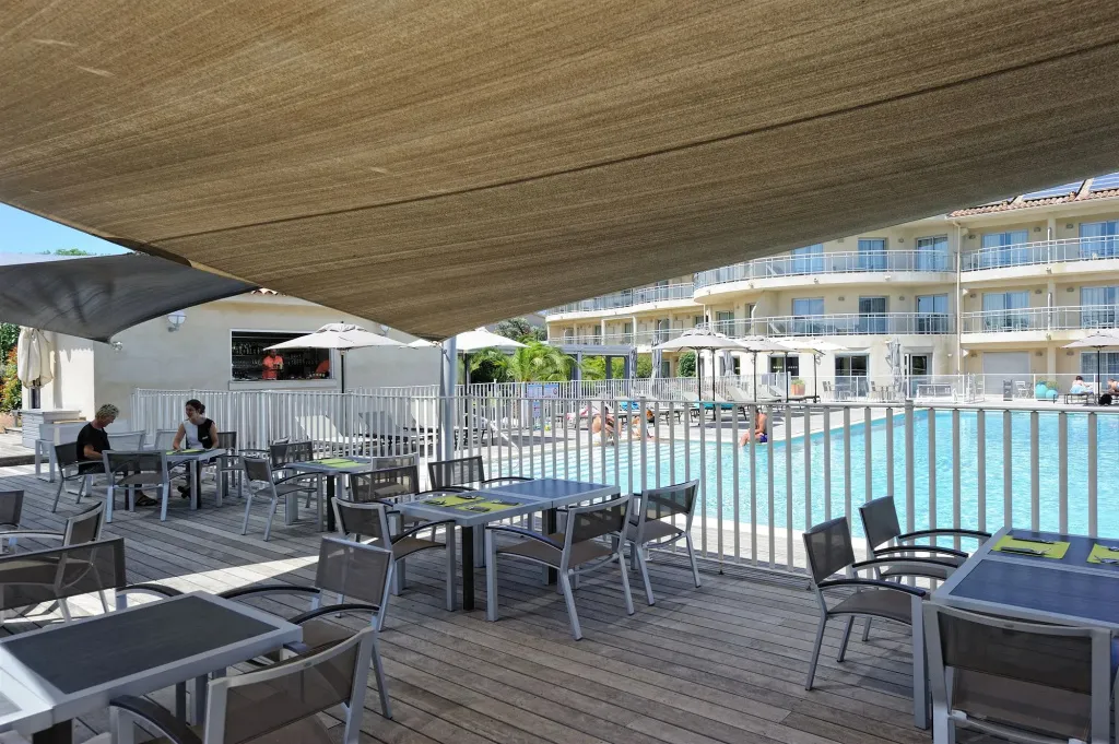 Terrasse ombragée avec tables et chaises près d'une piscine.