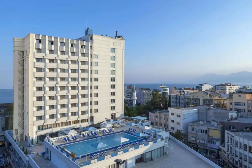 Bâtiment blanc à plusieurs étages avec une piscine sur le toit et vue sur la mer.