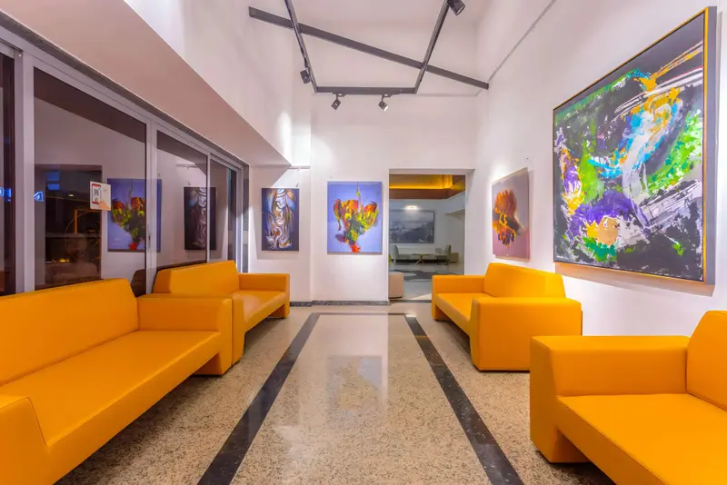 Espace de détente lumineux avec des canapés orange et des œuvres d'art colorées.