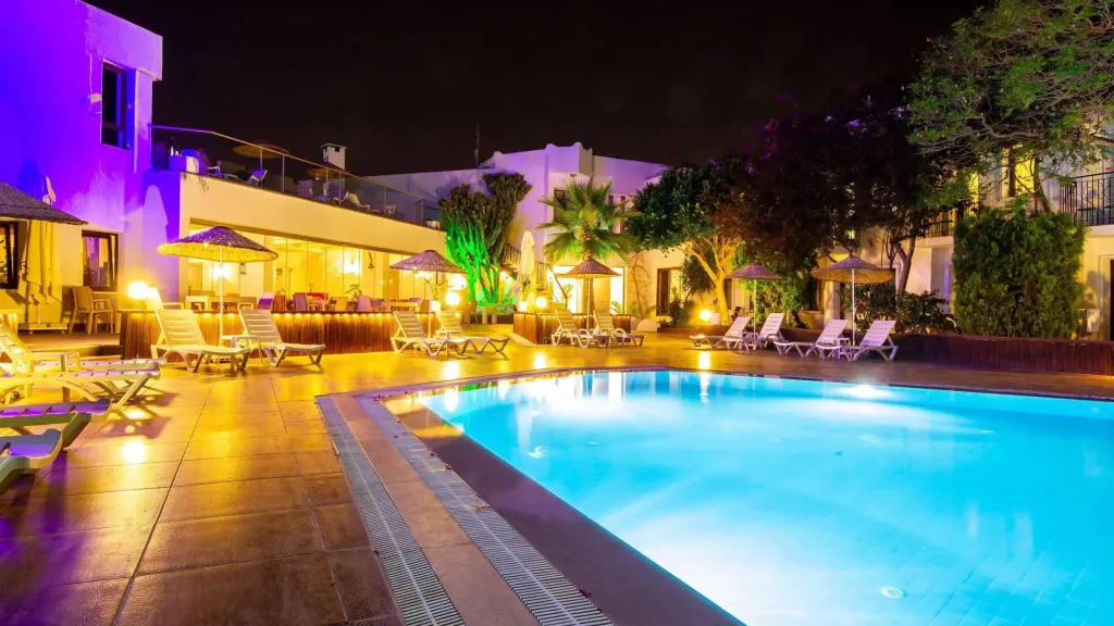 Piscine illuminée au crépuscule avec transats et végétation luxuriante.