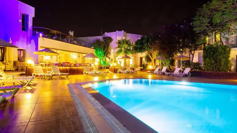 Piscine illuminée au crépuscule avec transats et végétation luxuriante.