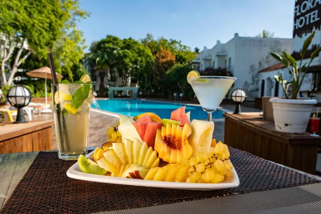 Une assiette de fruits frais et des boissons rafraîchissantes sont présentées sur une table près d'une piscine.