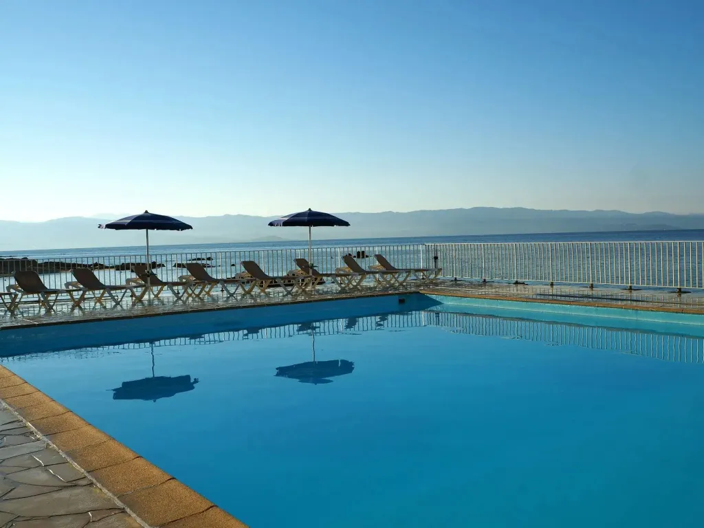 Une piscine bleu clair avec des transats et des parasols face à la mer.