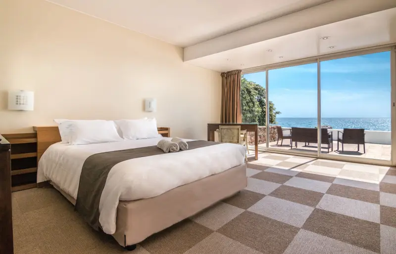 Une chambre lumineuse avec un grand lit donnant sur une terrasse et la mer.
