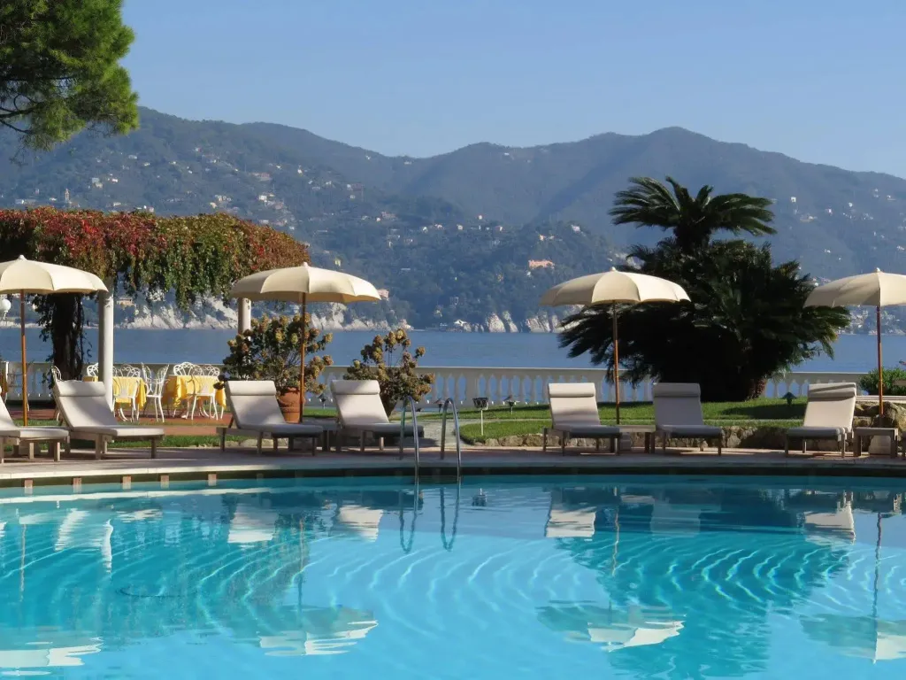 Une piscine turquoise avec des transats et des parasols, face à la mer et aux montagnes.