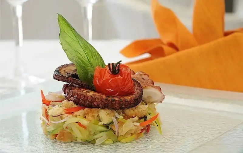 Assiette raffinée ornée de poulpe, de légumes et d'une feuille verte.