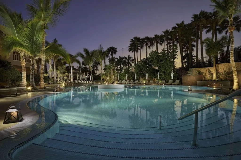 Une piscine illuminée au crépuscule, entourée de palmiers.