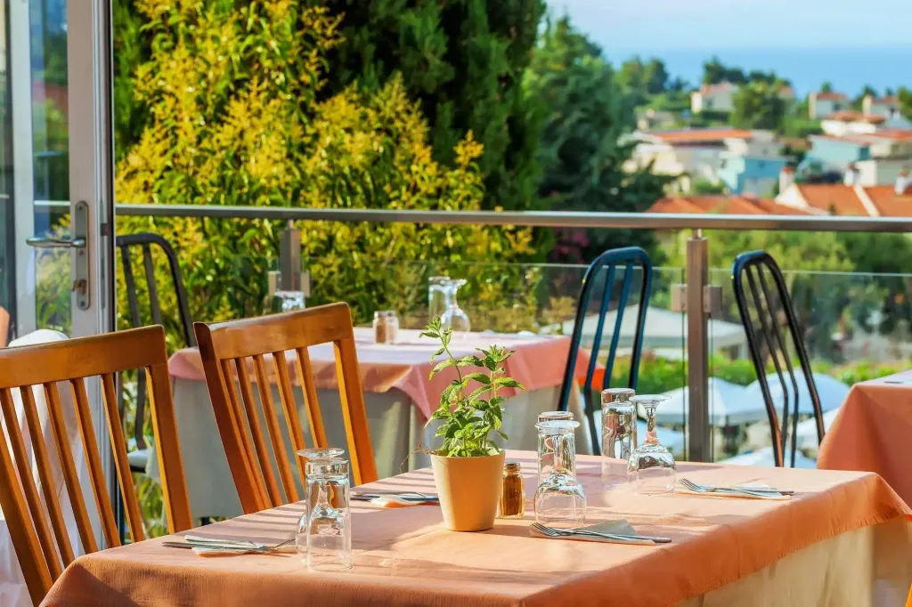 Tables dressées en terrasse avec vue sur la mer et la végétation.
