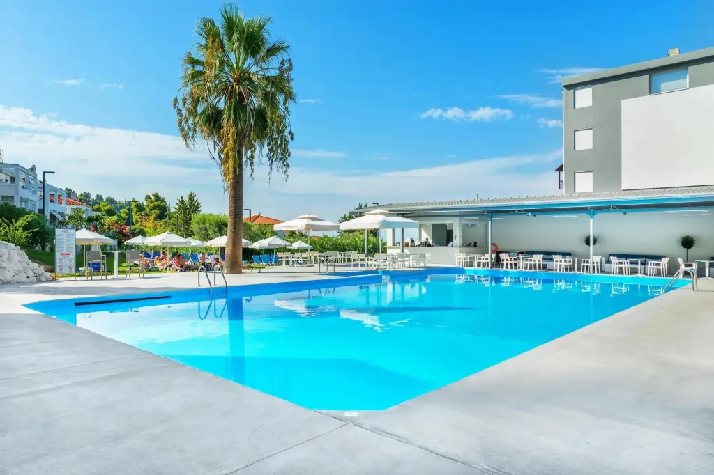 Une piscine rectangulaire bordée d'un sol carrelé et de transats sous des parasols.
