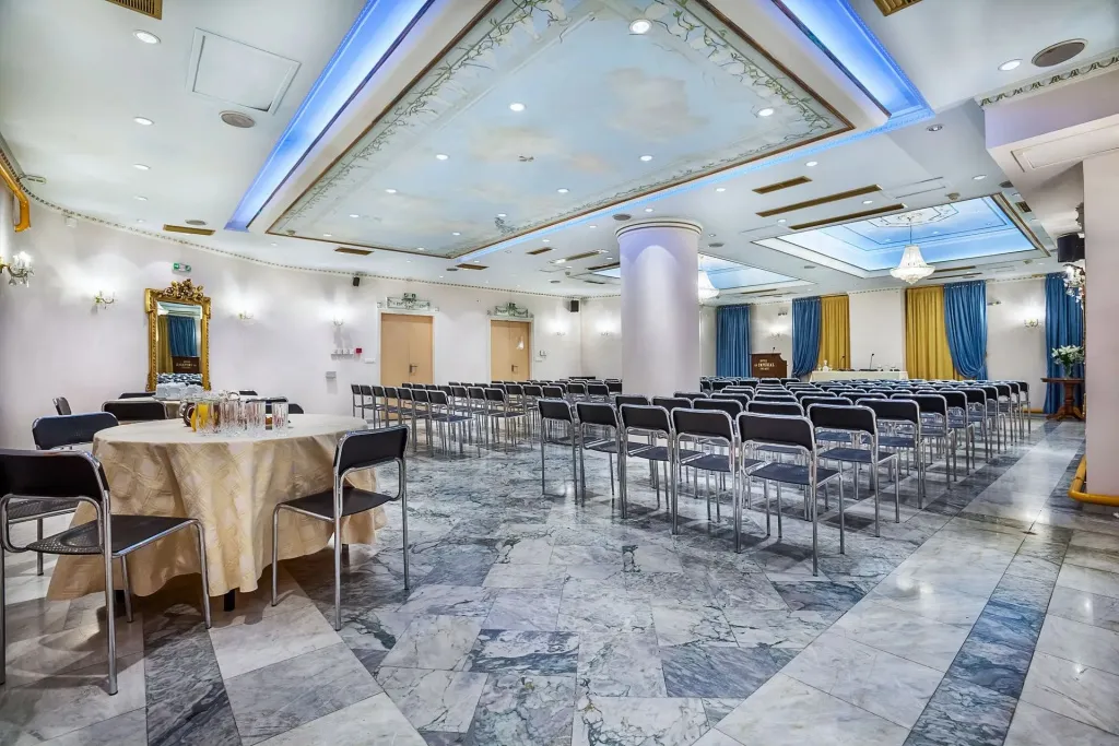 Une salle spacieuse est aménagée avec des tables rondes et de nombreuses chaises alignées.