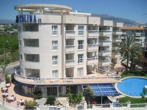 Bâtiment beige à plusieurs étages avec des balcons et une piscine en contrebas.
