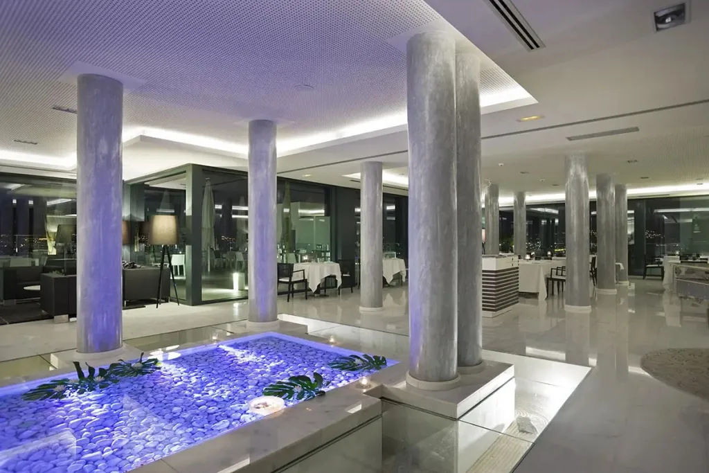 Une salle lumineuse avec des colonnes et une fontaine illuminée.