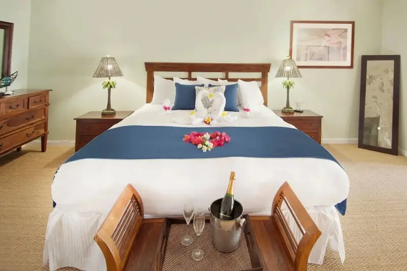 Une chambre lumineuse avec un grand lit décoré de fleurs et une bouteille de champagne.
