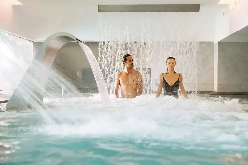 Un couple se détend dans une piscine intérieure avec un jet d'eau massant.