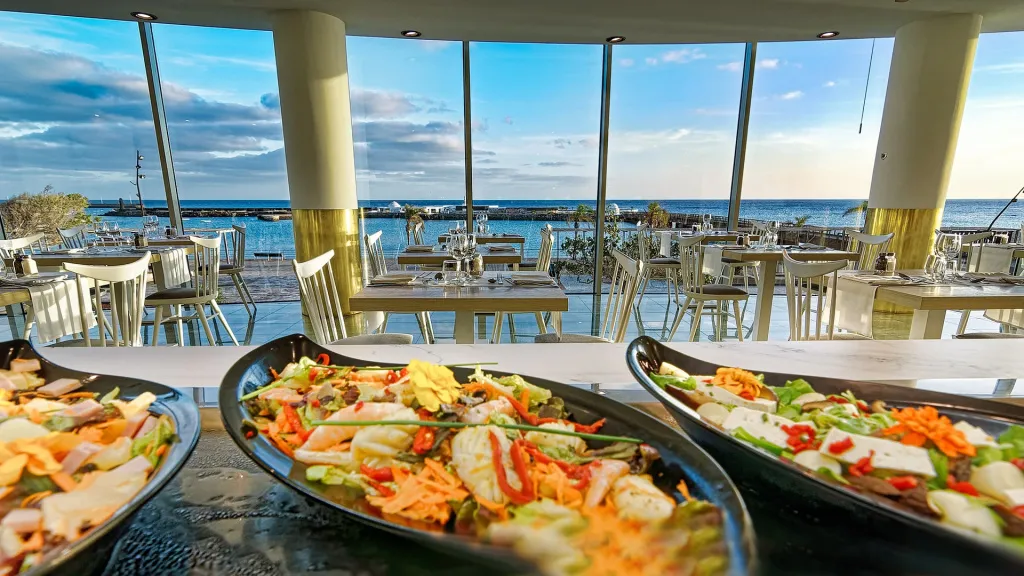 Des salades colorées sont présentées sur une table dans un restaurant lumineux avec vue sur la mer.