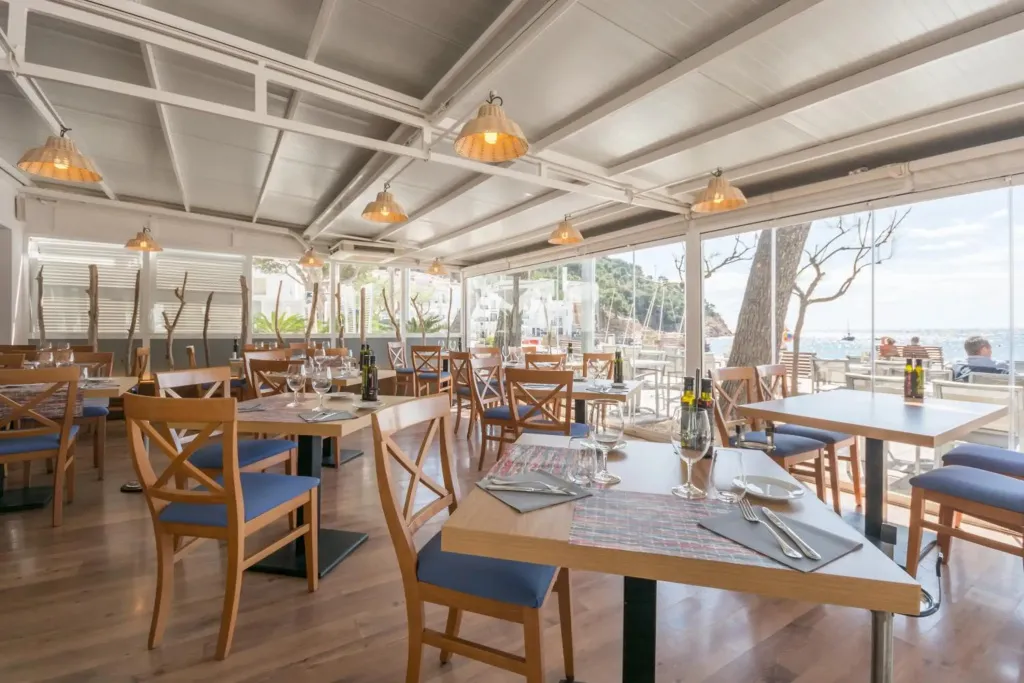 Une salle lumineuse avec des tables et des chaises près d'une grande baie vitrée donnant sur la mer.