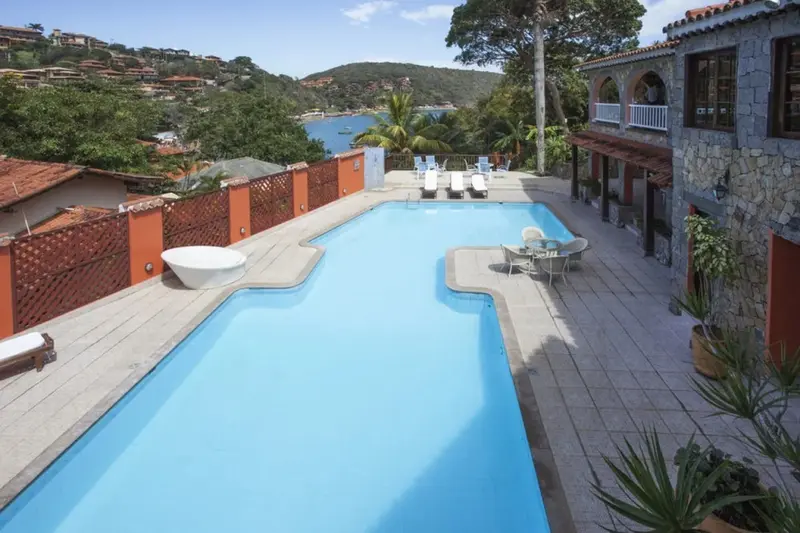 Une piscine rectangulaire bordée d'une terrasse ensoleillée offre une vue sur la mer et la végétation.