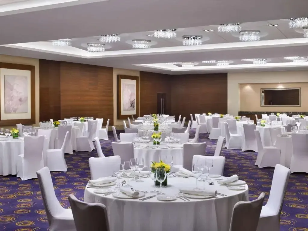 Une salle spacieuse est mise en scène avec des tables rondes nappées et des chaises habillées pour un événement.