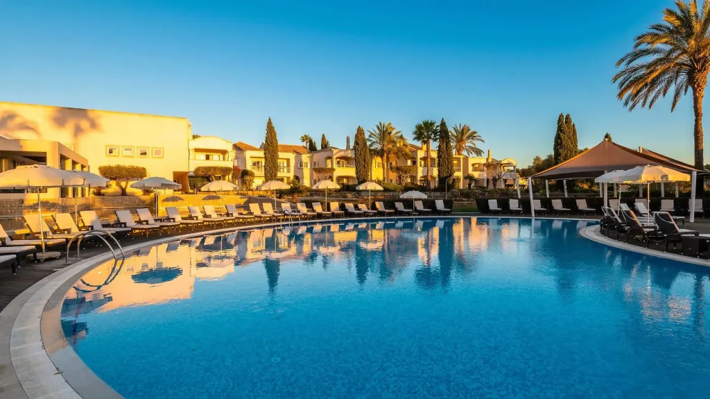 Une piscine rectangulaire bordée de transats sous le ciel bleu.