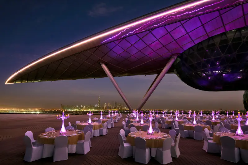 Tables rondes dressées pour un dîner en extérieur avec une vue sur la ville illuminée.