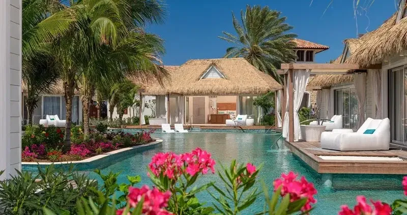 Des transats blancs invitent à la détente au bord d'une piscine turquoise ombragée par des palmiers.