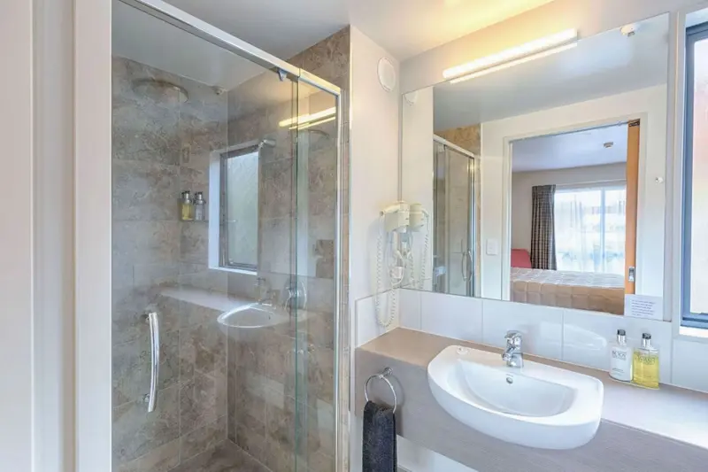 Une salle de bain lumineuse avec douche vitrée et vasque.