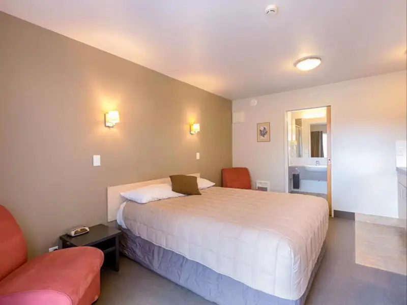 Une chambre lumineuse avec un lit double et un fauteuil.