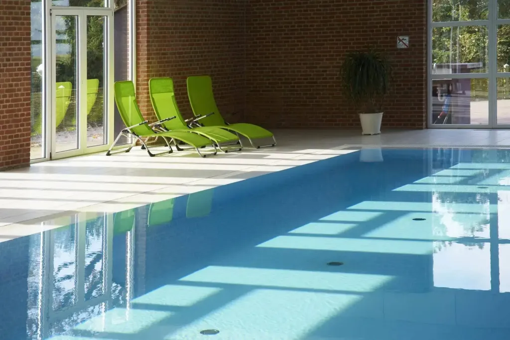 Transats verts au bord d'une piscine intérieure lumineuse.