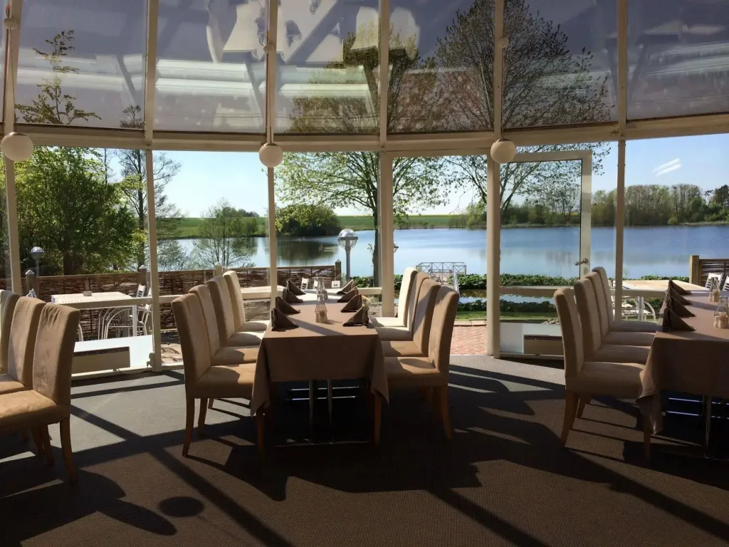 Une salle lumineuse avec des tables dressées face à un plan d'eau.