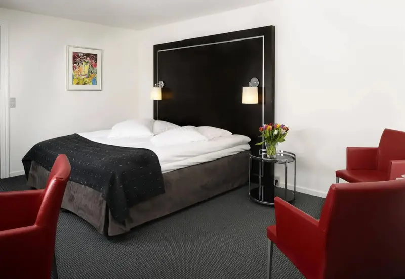 Une chambre moderne avec un grand lit et deux fauteuils rouges.