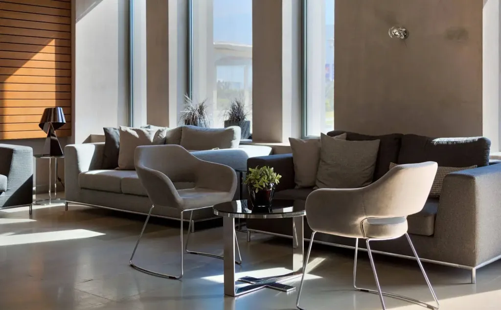 Espace de détente avec canapés et fauteuils près de grandes fenêtres.