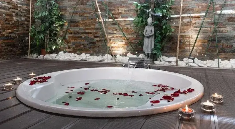 Baignoire ronde remplie d'eau et de pétales de fleurs, éclairée par des bougies.