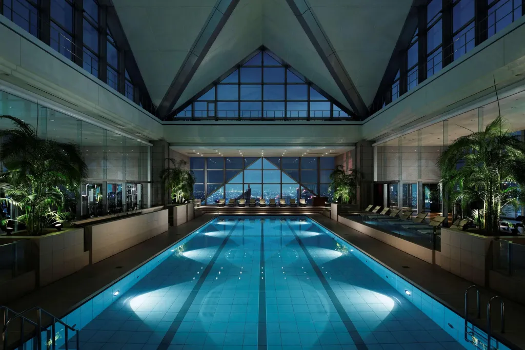 Une piscine intérieure lumineuse avec une vue sur la ville la nuit.