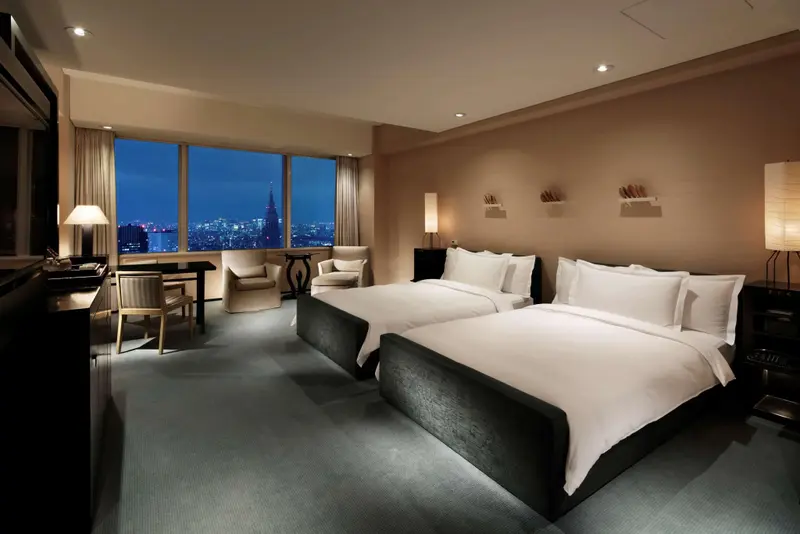 Chambre moderne avec deux lits et vue sur la ville illuminée.