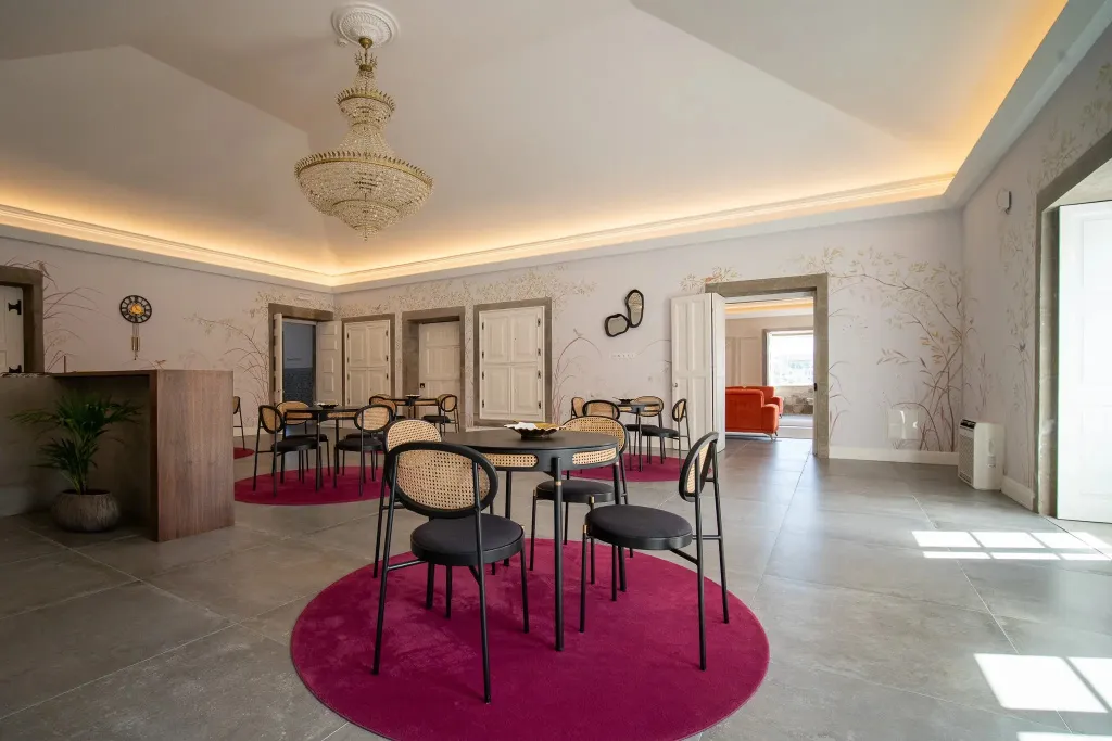 Une salle lumineuse avec des tables rondes et des chaises noires sur un tapis rose.