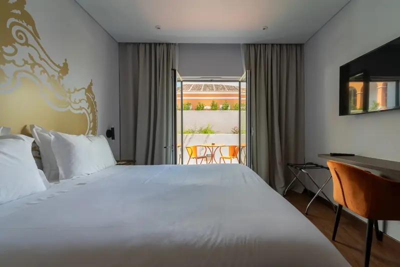 Une chambre lumineuse avec un grand lit et un bureau donnant sur une terrasse.
